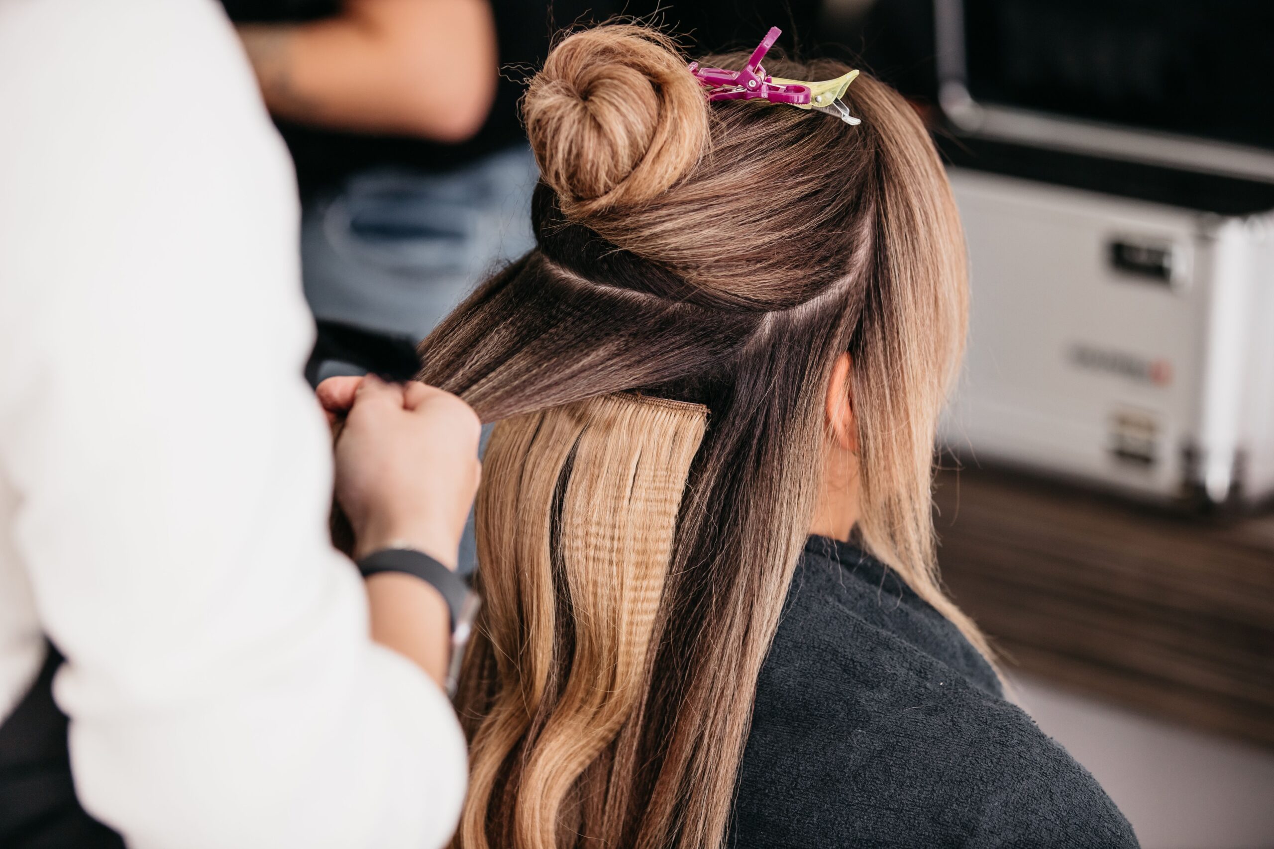 A young female with long wavy hair styling her locks using a straightener